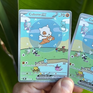 Op de afbeelding: Twee Cubone EX Pok&eacute;mon-ruilkaarten. De kaarten tonen een Cubone-personage met een bottenhelm en een lichtblauwe achtergrond. De kaarten hebben tekst als "Bone Smash" en "Beat".