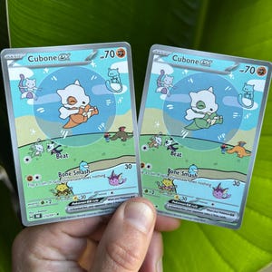 Op de afbeelding: Twee Cubone EX Pok&eacute;mon-verzamelkaarten. Elke kaart toont een wit Cubone-personage met een oranje bottenknuppel, tegen een blauwgroene achtergrond. De kaarten hebben de tekst "Beat" en "Bone Smash".