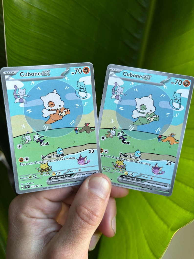Op de afbeelding: Twee Cubone EX Pok&eacute;mon-verzamelkaarten. Elke kaart toont een wit Cubone-personage met een oranje bottenknuppel, tegen een blauwgroene achtergrond. De kaarten hebben de tekst "Beat" en "Bone Smash".