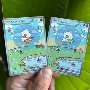 Op de afbeelding: Twee Cubone EX Pok&eacute;mon-verzamelkaarten. Elke kaart toont een wit Cubone-personage met een oranje of groene bottenknuppel. De kaarten hebben een blauwgroene achtergrond met de tekst "Beat" en "Bone Smash".