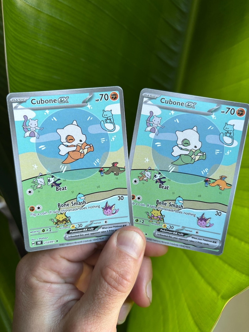 Op de afbeelding: Twee Cubone EX Pok&eacute;mon-verzamelkaarten. Elke kaart toont een wit Cubone-personage met een oranje of groene bottenknuppel. De kaarten hebben een blauwgroene achtergrond met de tekst "Beat" en "Bone Smash".