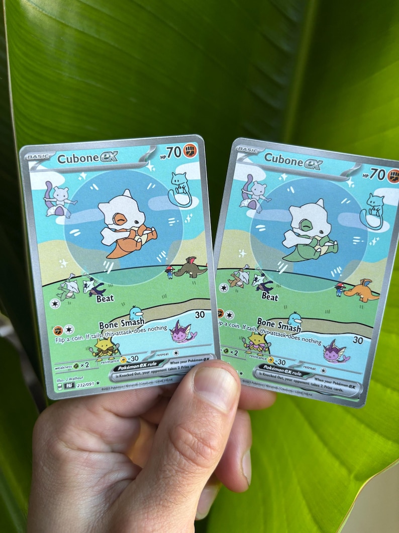 Op de afbeelding: Twee Cubone EX Pok&eacute;mon-verzamelkaarten. Elke kaart toont een cartoon Cubone-personage met een oranje of groene outfit, tegen een achtergrond van blauwe lucht en groen gras. De kaarten hebben 70 HP.