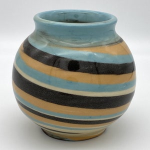 May include: A round ceramic vase with a blue, white, black, and orange striped pattern.