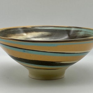 May include: A large ceramic bowl with a wide, flared rim and a narrow base. The bowl is decorated with a swirling pattern of black, blue, and yellow stripes.