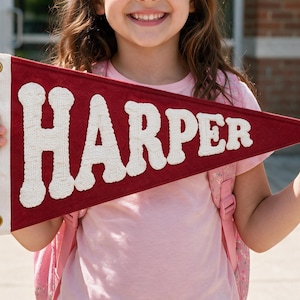 Puede incluir: Un banderín triangular de fieltro granate con el nombre HARPER en letras mayúsculas blancas grandes y texturizadas. El banderín tiene una franja vertical blanca en el lado izquierdo con dos ojales metálicos de color latón.