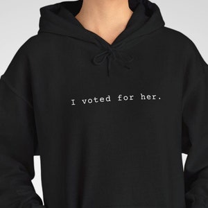 Op de afbeelding: Zwart hoodie met de tekst "I voted for her." in wit gedrukt op de voorkant.