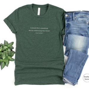 May include: A green t-shirt with the text 'I yield for a question while retaining the floor Cory Booker' printed on the front.