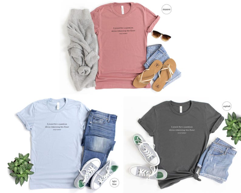 May include: Three t-shirts in different colors: mauve, light blue, and asphalt. Each t-shirt has the same text printed on the front: 'I paid for a vacation while relaxing on the floor. Stay Home.' The t-shirts are displayed on a white background with jeans, sandals, and a sweater.