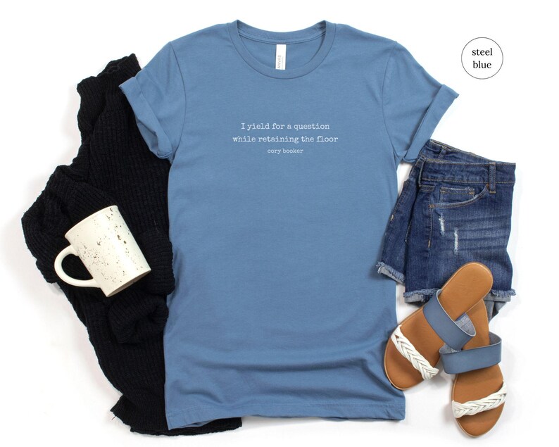 May include: A steel blue t-shirt with the text 'I yield for a question while retaining the floor Cory Booker' printed on the front.