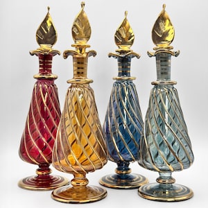 Peut inclure: Quatre flacons décoratifs en verre rouge, or, bleu et sarcelle. Chaque flacon présente un motif en spirale avec des accents dorés et un bouchon doré en forme de feuille. Les flacons ont une base ronde avec une bordure dorée.