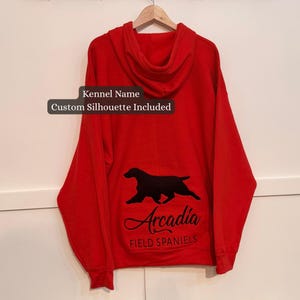 Może przedstawiać: Czerwona bluza z kapturem z czarną sylwetką psa i napisem "Arcadia" w ozdobnej czcionce. Tekst "Field Spaniels" znajduje się poniżej. Tekst "Kennel Name Custom Silhouette Included" znajduje się nad sylwetką psa.