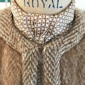 May include: A brown and white fuzzy sweater with a brown and white checkered scarf tied around the neck.