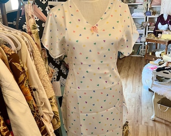 May include: A white satin nightgown with a V-neckline and short sleeves. The nightgown is covered in a pattern of colorful hearts. The nightgown is on a mannequin in a shop.