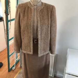 May include: A brown fuzzy jacket with a white and brown trim, worn over a white and brown patterned blouse and a brown skirt.