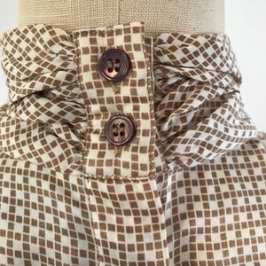May include: A white blouse with a brown geometric pattern and a ruffled collar. The collar has two brown buttons.
