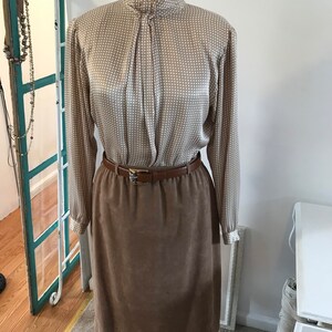 May include: A brown suede skirt with a brown leather belt and a white and brown patterned blouse with a high collar.