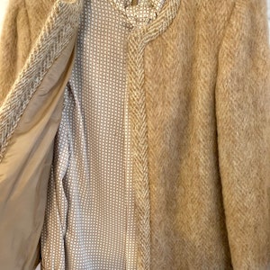 May include: A brown tweed jacket with a herringbone pattern and a matching skirt. The jacket is open to reveal a white and brown patterned blouse.