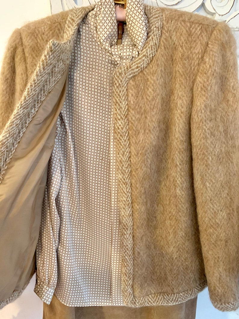 May include: A brown tweed jacket with a herringbone pattern and a matching skirt. The jacket is open to reveal a white and brown patterned blouse.