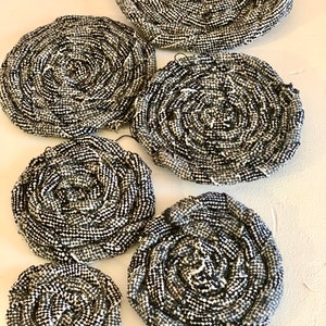 Puede incluir: Un conjunto de siete posavasos circulares tejidos en blanco y negro. Los posavasos están hechos de una tela gruesa y texturizada y están dispuestos en orden descendente de tamaño.