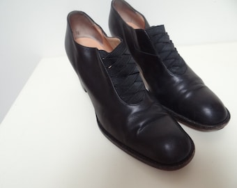 May include: A pair of black leather heeled shoes with a black ribbon lacing detail across the vamp.