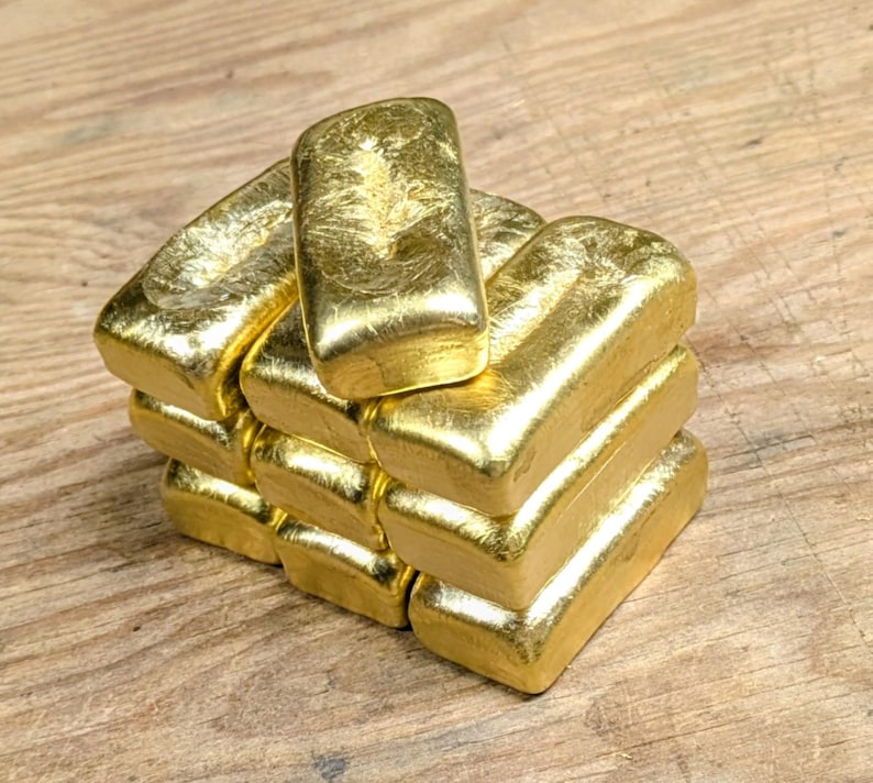 May include: A stack of gold bars, each with a rectangular shape and a shiny, textured surface. The bars are arranged in a staggered formation, creating a visually appealing display. The gold color is bright and reflective.