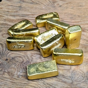 May include: A collection of gold bars, each with a rectangular shape and a shiny, reflective surface. The bars are arranged on a wooden surface, creating a display of wealth and value. The gold bars are a symbol of investment and financial security.