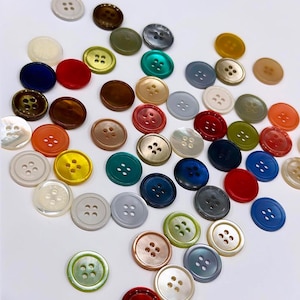 Puede incluir: Surtido de botones coloridos en varios tonos de azul, verde, rojo, naranja, amarillo, marrón y blanco. Los botones son redondos y tienen cuatro agujeros.