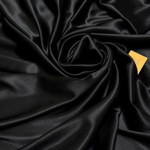 May include: Black satin fabric with a smooth, silky texture. The fabric is draped and folded, creating soft curves and folds.