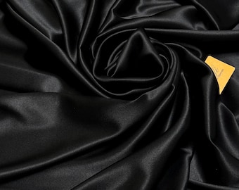 May include: Black satin fabric with a smooth, silky texture. The fabric is draped and folded, creating soft curves and folds.