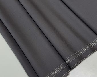 May include: A folded bolt of dark gray fabric with a subtle woven texture. The fabric has a white border with the text "LANA VERGINE" printed on it. The fabric is neatly folded, showcasing its smooth surface.
