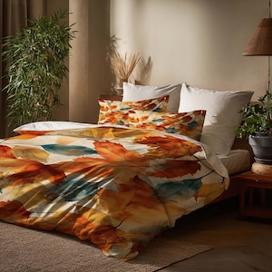 May include: A bed with a duvet cover and pillowcases featuring a large leaf pattern in shades of orange, yellow, and teal. The bedding is on a wooden bed frame, with a neutral-toned rug and a potted plant in the background.
