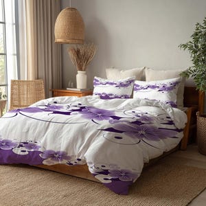 Puede incluir: Juego de cama blanco con un gran diseño floral púrpura. El juego incluye una funda nórdica y dos fundas de almohada. Las flores tienen un diseño detallado con acentos arremolinados. La cama tiene un marco de madera y está sobre una alfombra tejida.