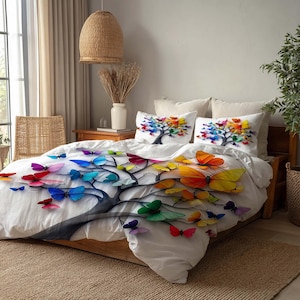 Op de afbeelding: Witte beddengoedset met een boom- en vlinderontwerp. Het dekbedovertrek en de twee kussenslopen tonen een boom met kleurrijke vlinders in rood, oranje, geel, groen, blauw en paars. Het bed is van hout.