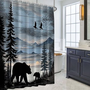 May include: A shower curtain featuring a printed landscape of a black bear and cub in a forest with tall pine trees, distant mountains, a setting sun, and two birds flying against a blue and grey wood-plank textured background.