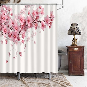May include: A white shower curtain featuring a printed pattern of pink cherry blossom branches extending from the top left corner. The design includes numerous blooming flowers in various shades of pink and dark brown stems on a plain white background.
