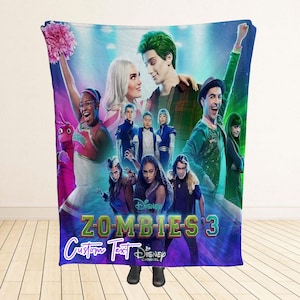May include: A large, rectangular blanket with a vibrant graphic from the Disney Channel film "Zombies 3." The design showcases characters, the movie title, and the words "Custom Text" in a decorative font. The blanket is shown against a white backdrop.