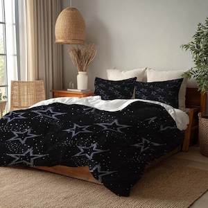 Pode incluir: Conjunto de roupa de cama preto com padrão de estrelas. A capa de edredão e as fronhas apresentam grandes estrelas delineadas e pequenos pontos brancos sobre um fundo preto. A cama é feita com um lençol branco.