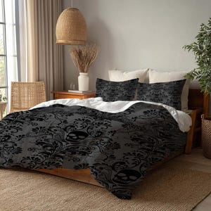 May include: A bed with a black and gray skull-themed comforter set. The comforter and two pillowcases feature a repeating skull and floral pattern. The bed is made up with white sheets and is on a wooden bed frame.