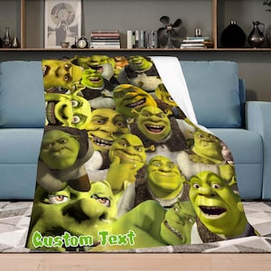 Può includere: Una coperta in pile verde con un collage del volto di Shrek. La coperta ha un retro bianco e le parole "Custom Text" in verde. La coperta è drappeggiata su un divano blu.