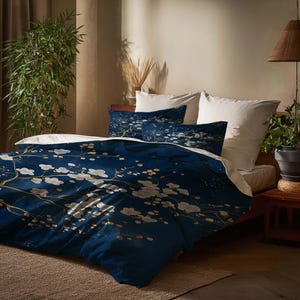 May include: A navy blue duvet cover and pillowcases with a white floral design. The bedding set features a dark blue background with white flowers and gold-coloured branches. The bed is made with white sheets.