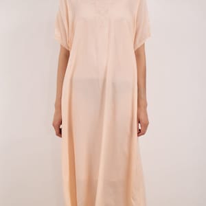 Peut inclure: Une robe ample de couleur rose pâle, de longueur genoux, avec un col en V et des manches courtes. La robe est ornée d'un délicat motif brodé sur le devant.