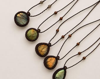 Puede incluir: Cinco collares con piedras preciosas de labradorita pulidas en engastes de macramé marrón oscuro. Las piedras varían entre formas redondas y de lágrima, mostrando destellos iridiscentes dorados, verdes y azules. Cada cordón incluye cuentas.