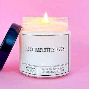 Può includere: Una candela bianca accesa in un barattolo di vetro con coperchio nero. La candela ha il testo "BEST BABYSITTER EVER" sul davanti. La candela è etichettata "SPICY WAX CANDLE" e "CANDELA IN CERA DI SOIA COLATA A MANO IN ITALIA".