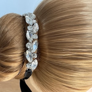 May include: A hair accessory featuring a row of clear rhinestones set in silver metal. The accessory is attached to a black ribbon.