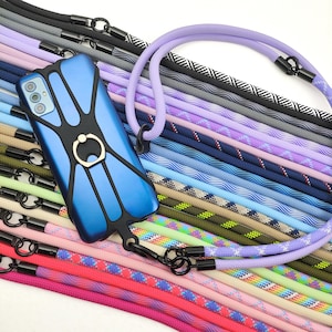 May include: A blue phone case with a black frame and a gold ring holder, displayed with a variety of colorful phone lanyards. The lanyards are made of braided rope in various colors and patterns, including black, purple, and pink.