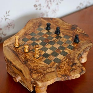 May include: A wooden chess set with a natural, organic edge. The chessboard features a checkerboard pattern with dark and light squares. The chess pieces are black and light brown. The set is displayed on a dark brown surface.