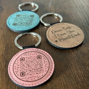 Peut inclure: Porte-clés ronds en cuir de différentes couleurs, dont rose, bleu et marron. Certains ont des codes QR, d'autres le message "Drive Safe I Love You Mom & Dad". Chaque porte-clés est doté d'un anneau argenté.