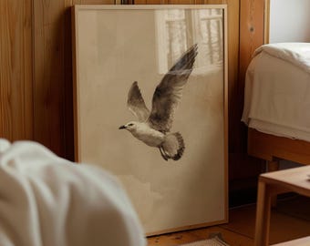 May include: A framed print of a seagull in flight. The artwork features a detailed illustration of the bird with outstretched wings, rendered in shades of gray and white against a neutral background. The frame is a light wood color, and the print is displayed in a room with wooden paneling.