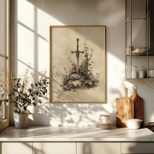 Peut inclure: Une impression encadr&eacute;e repr&eacute;sentant une &eacute;p&eacute;e dans une pierre, entour&eacute;e de verdure. L'&oelig;uvre est en tons s&eacute;pia, avec un cadre dor&eacute;. L'impression est expos&eacute;e dans une cuisine, &eacute;clair&eacute;e par la lumi&egrave;re naturelle.
