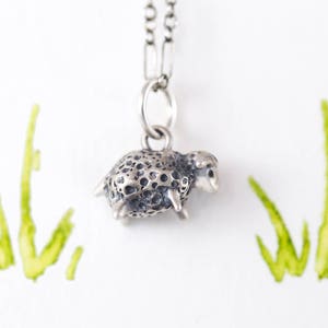 Puede incluir: Un collar de plata con un pequeño dije de oveja detallado. La oveja es texturizada y tiene una apariencia realista.